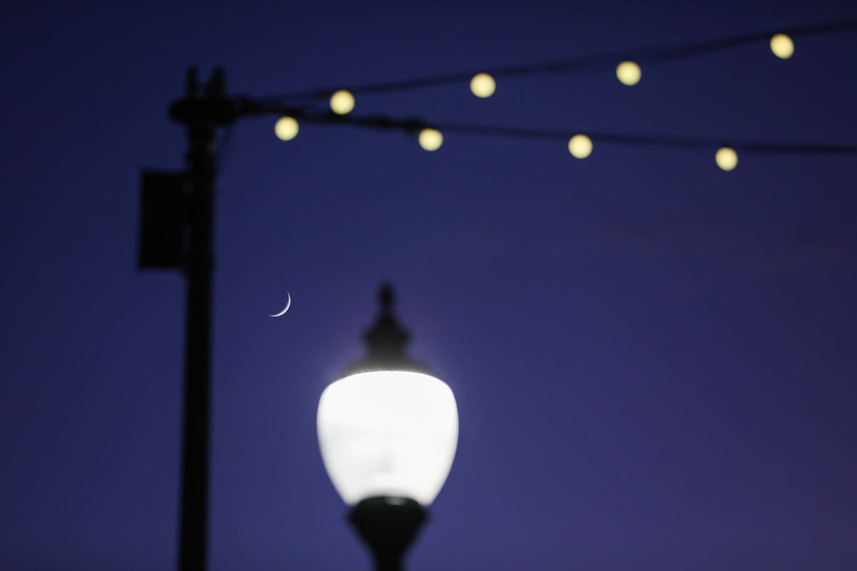 The moon sets behind a street light that is in the process of being retrofitted to give off les ...